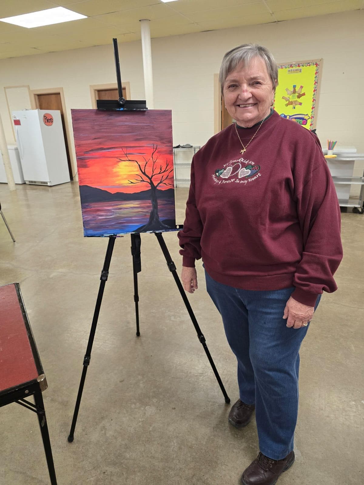 Paint night instructor standing proudly beside the evening's sunset painting on an easel